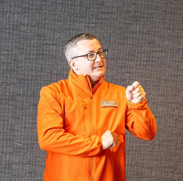 A person wearing glasses and an orange jacket with the text