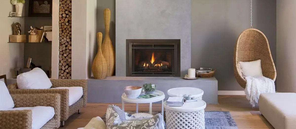 Modern living room with a fireplace, wicker chairs, a hanging wicker chair, and a wooden side table with decor items. Firewood is stacked beside the fireplace, and shelves hold decorative items.