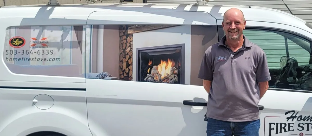 A man stands smiling in front of a white van with a fireplace image and text that includes a phone number and website for homefirestove.com. The van also features logos for Lopi and Fireplace Pro.