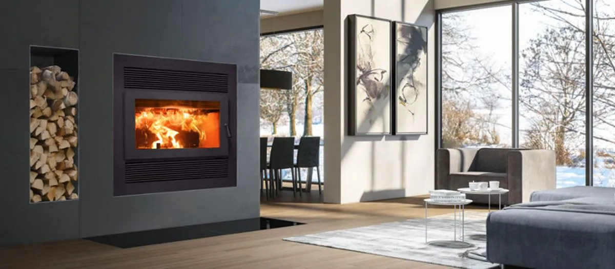 Modern living room with large windows showing a snowy outdoor scene. Features a built-in wood-burning fireplace, wood storage, abstract wall art, and minimalist furniture.