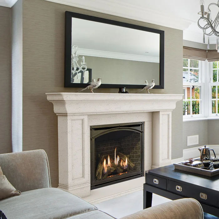 A modern living room with a lit fireplace. A large mirror is above the fireplace with two decorative birds on the mantle. Windows and a chandelier are in the background.