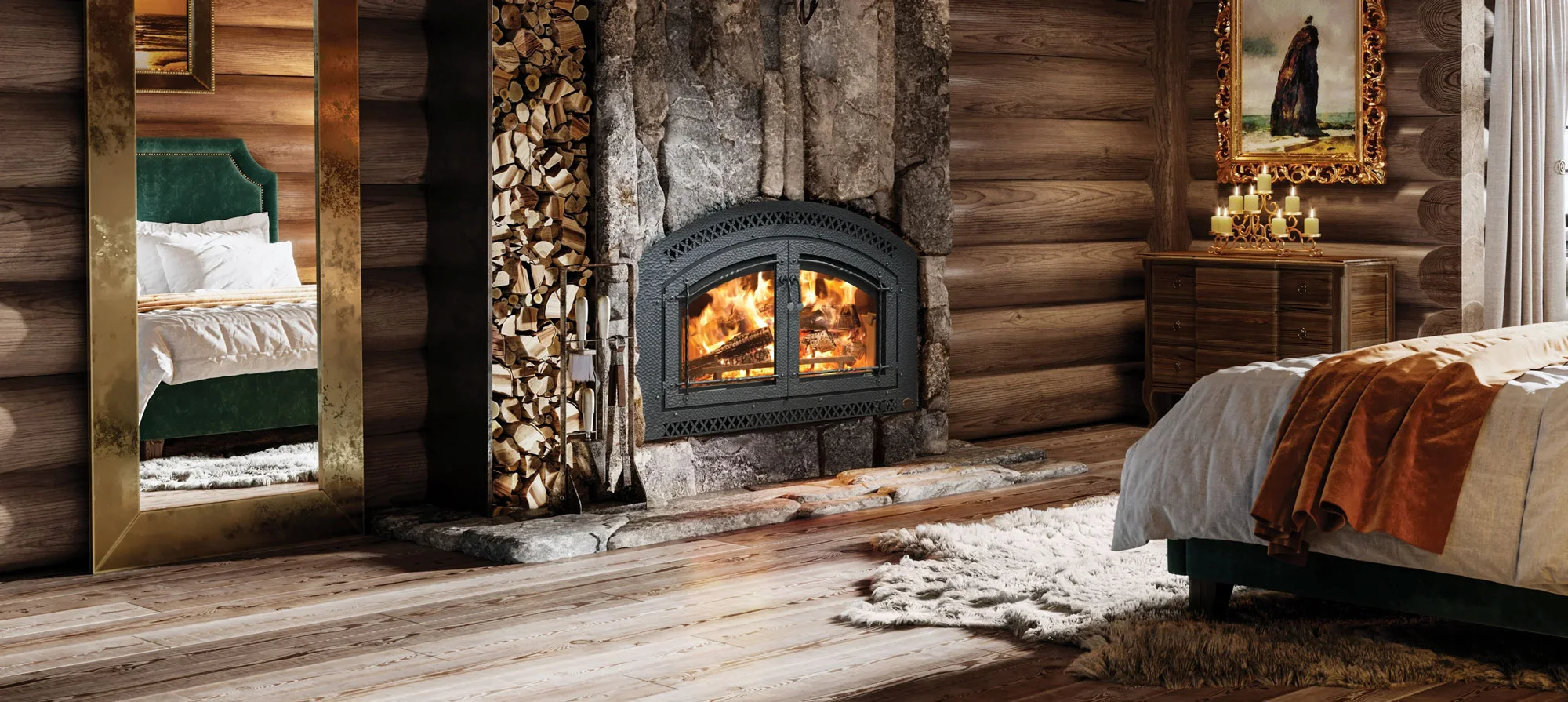 A cozy log cabin bedroom with a burning fireplace, woodpile, and mirror reflecting a bed with green headboard. A dresser with candles and a framed painting decorates the corner.