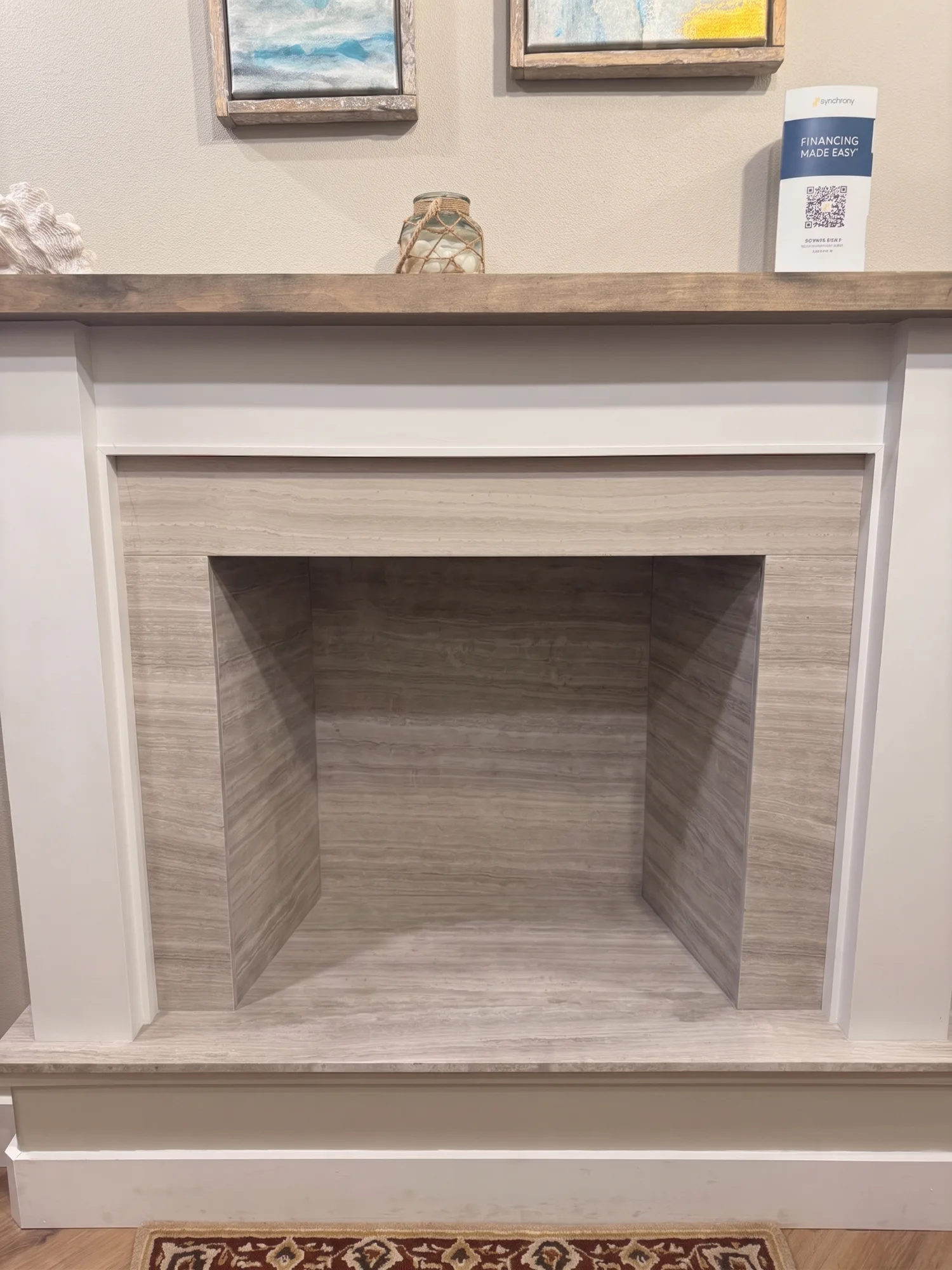 Empty modern fireplace niche with wood-look tile interior, white mantel and small decor items on shelf