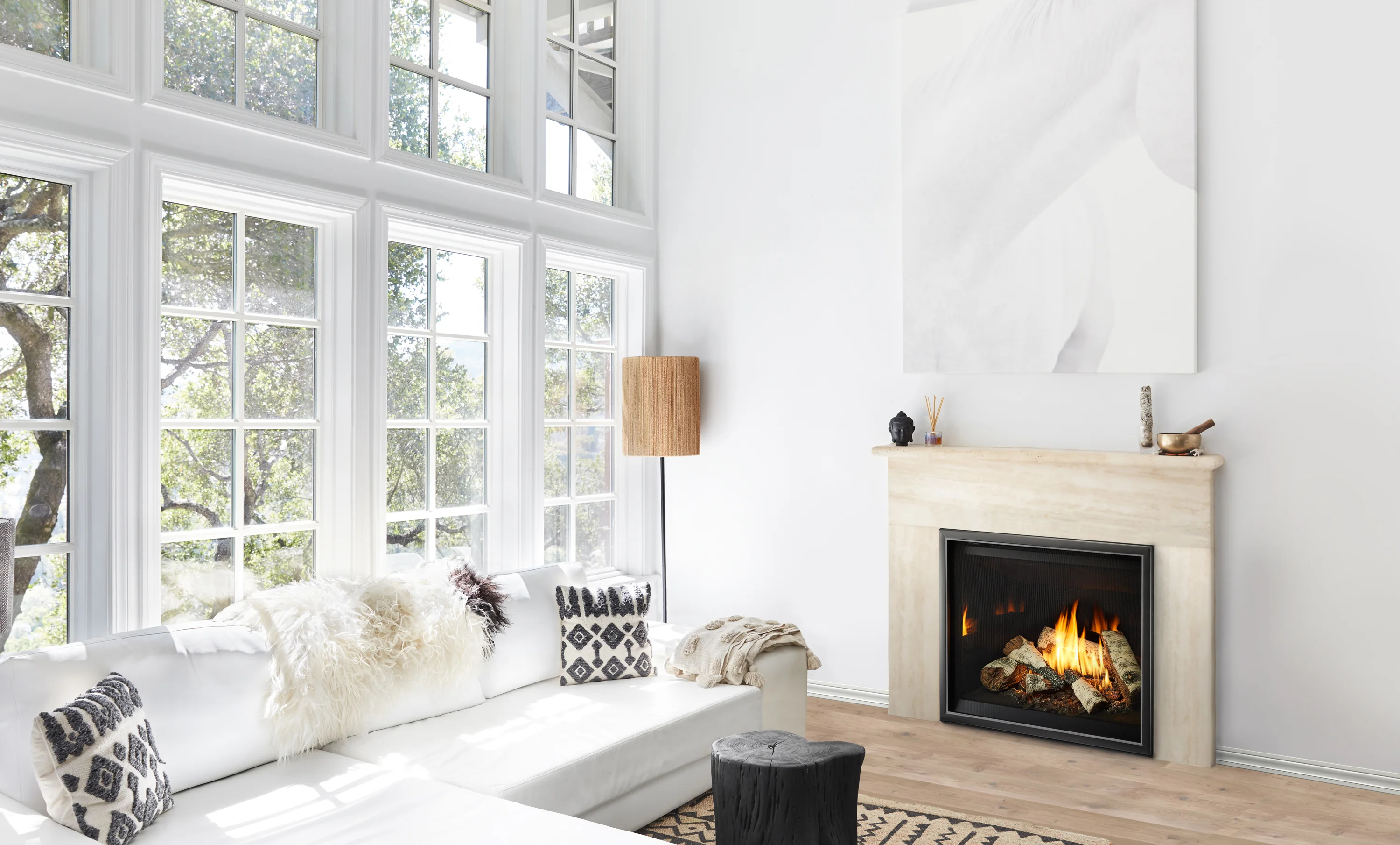 Bright modern living room with large multi-pane windows, white sectional sofa with textured pillows and throws, lit fireplace and a tall woven floor lamp