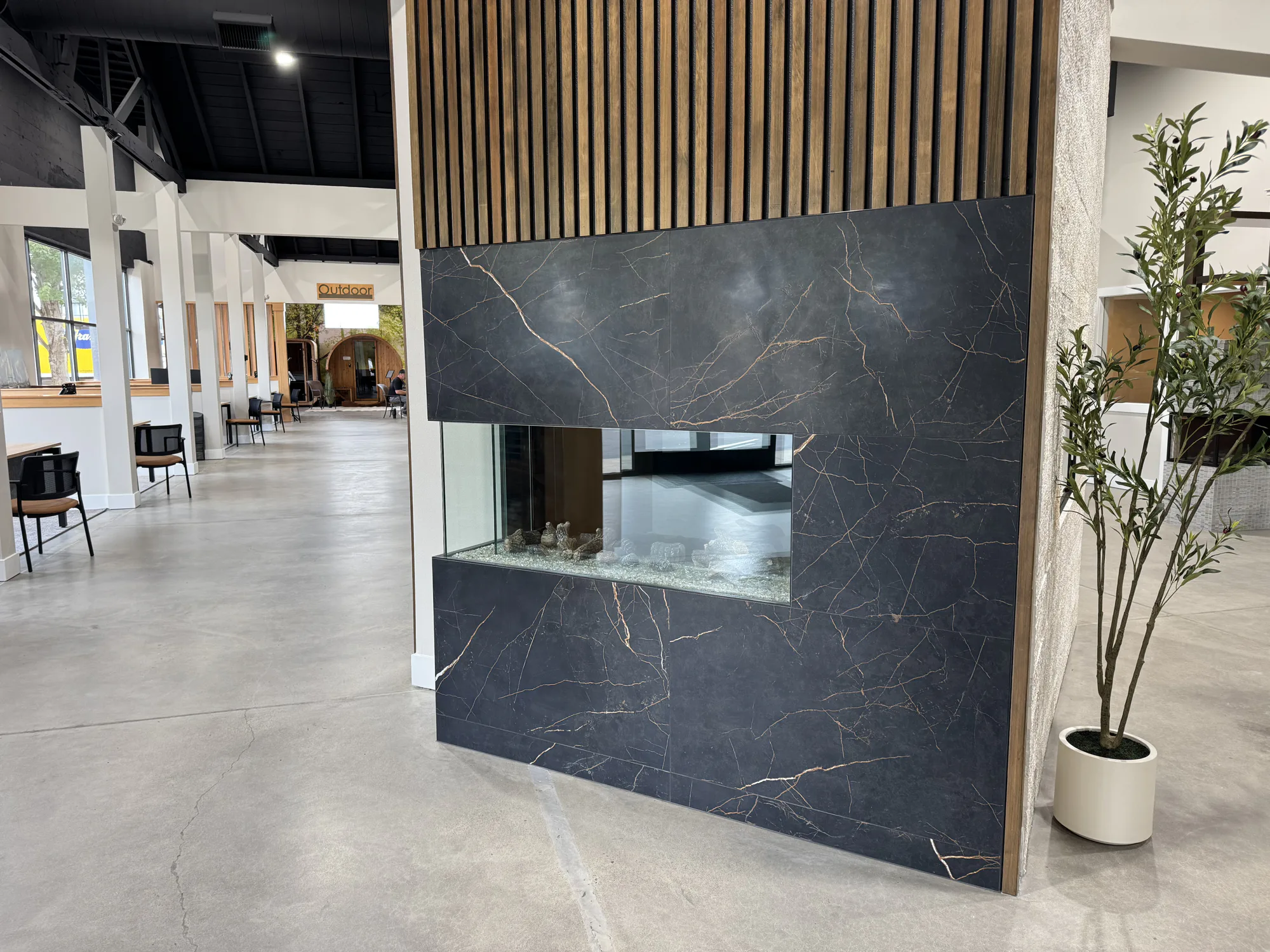 Interior showroom with a black marble double-sided fireplace, wood slats above, seating area and potted plant