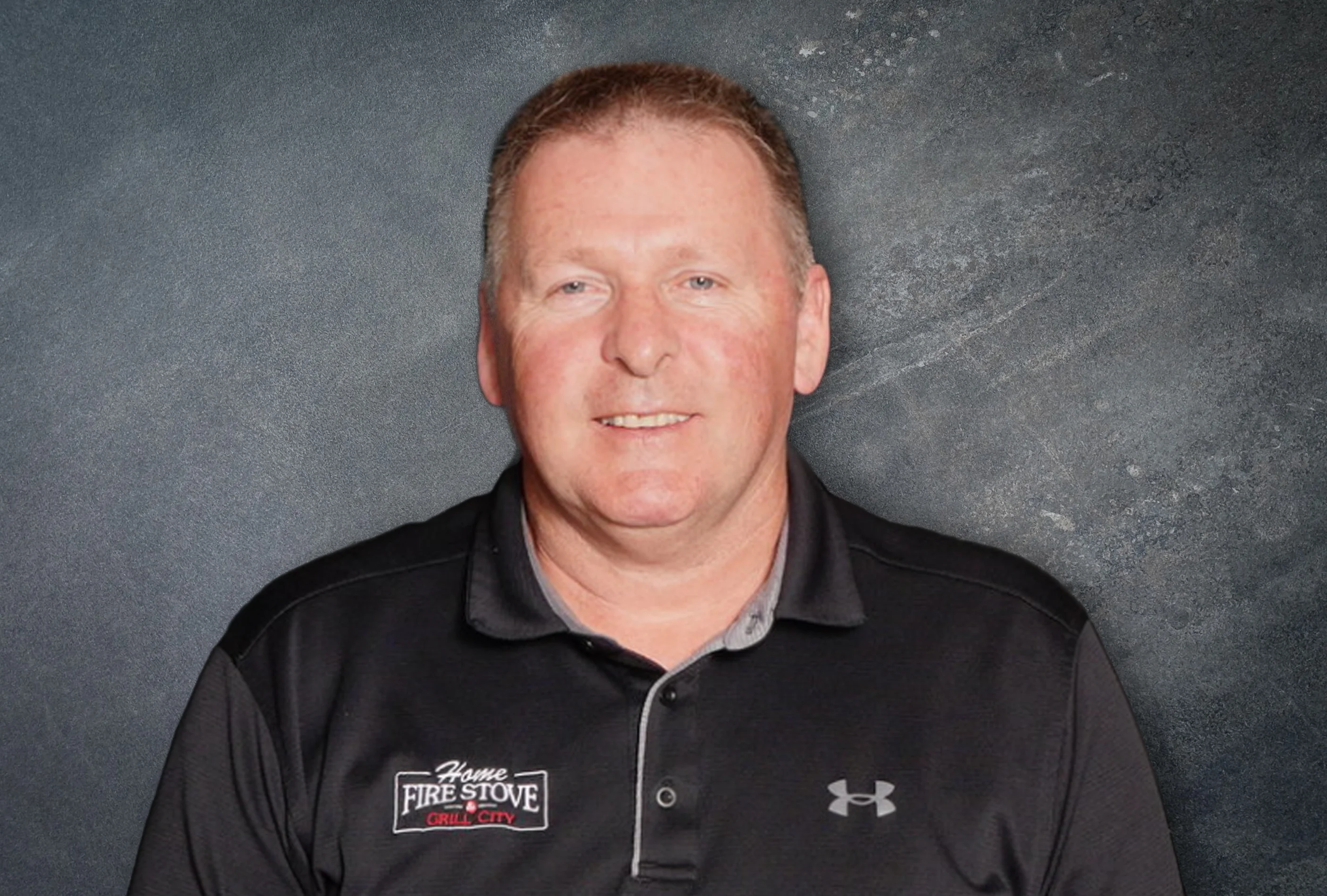Jeff Reynolds, owner of Home Fire Stove,  wearing a black polo shirt with Home Fire Stove Grill City logo, standing against a textured dark gray background.