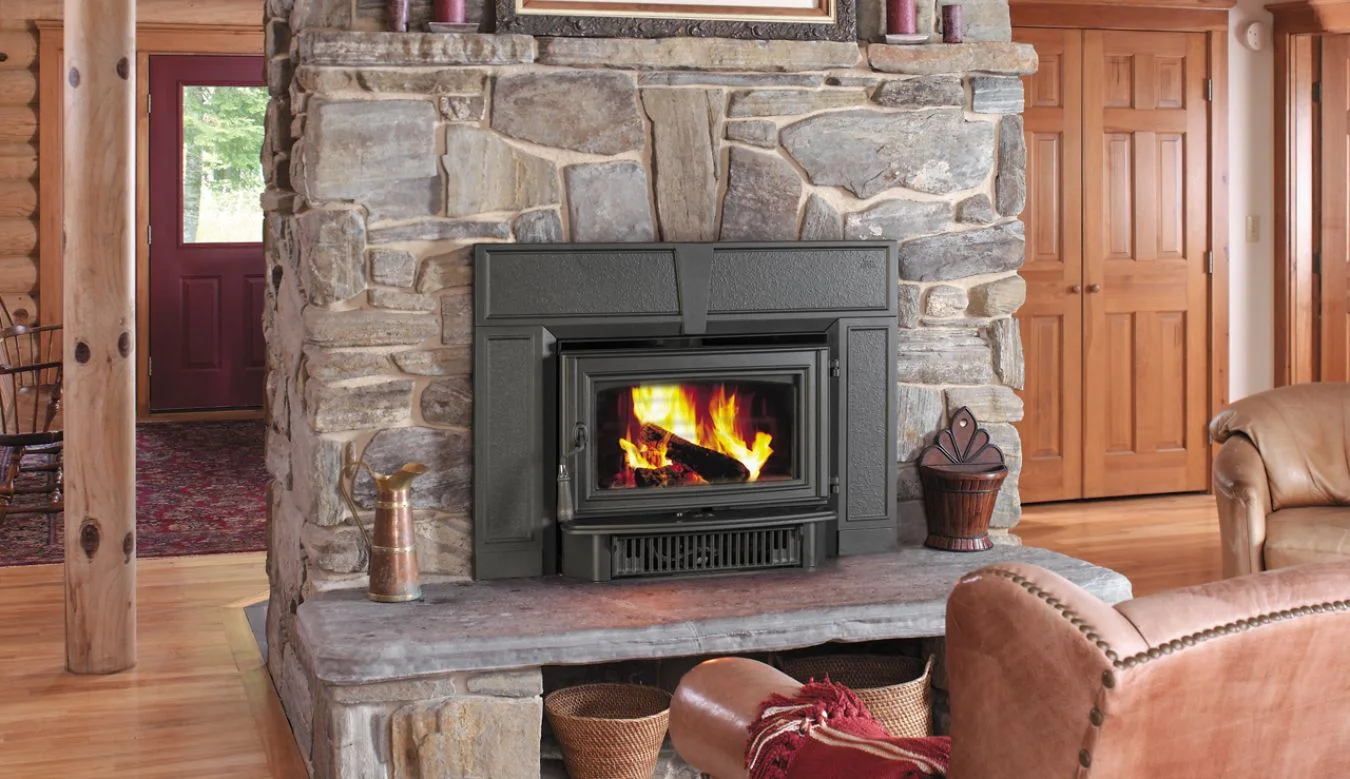 Stone fireplace with a blazing fire, surrounded by a rustic log cabin interior. Red door, wooden floors, leather chair, and a red, patterned rug are visible in the cozy room.