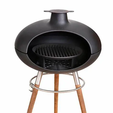 A modern black outdoor pizza oven with a rounded design on a tripod stand made of wooden legs and a metal support ring. The oven has a grill inside and is photographed against a white background.