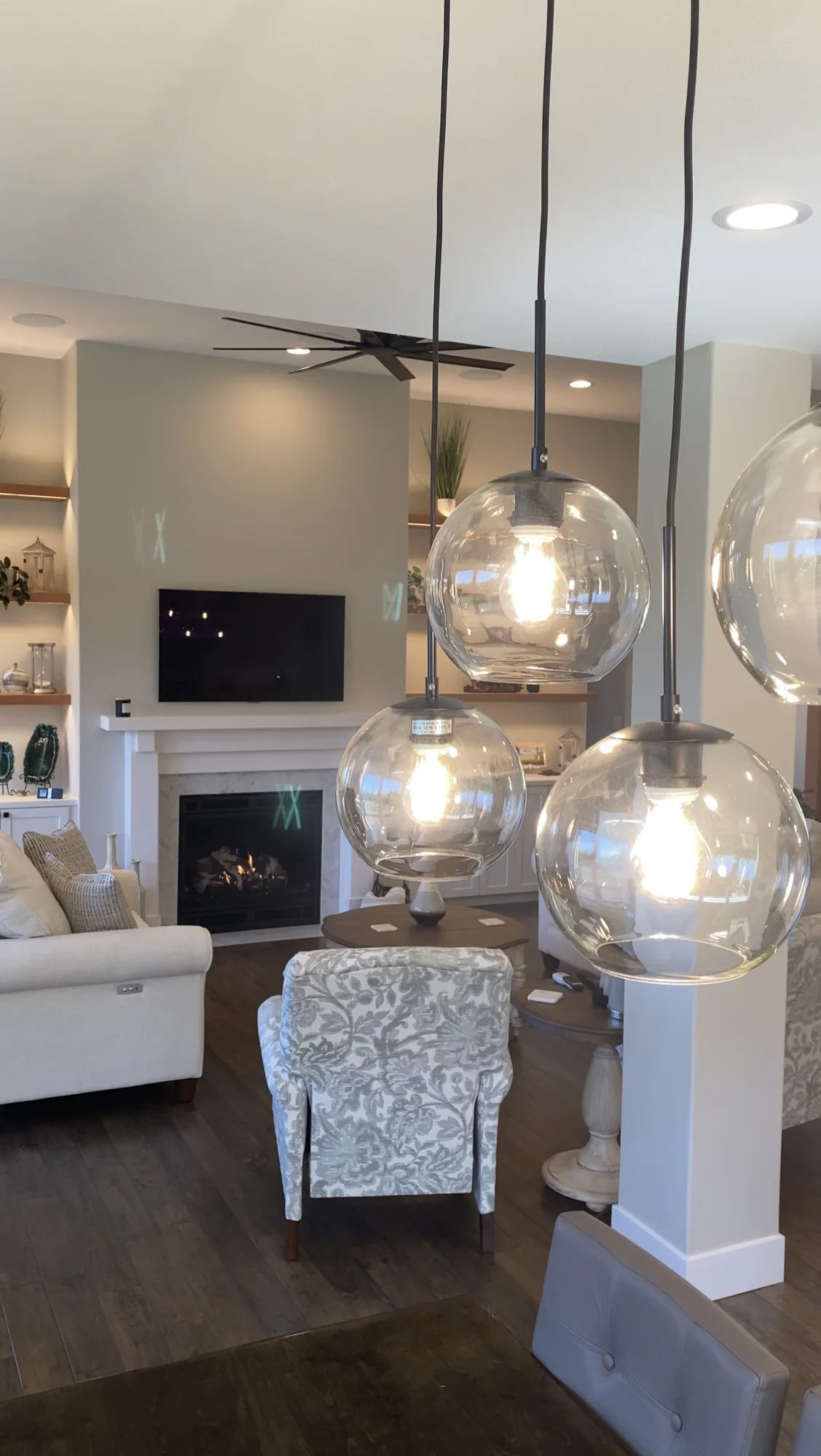 Modern living room with three glass globe pendant lights in foreground, patterned armchair, sofa, fireplace and wall-mounted TV