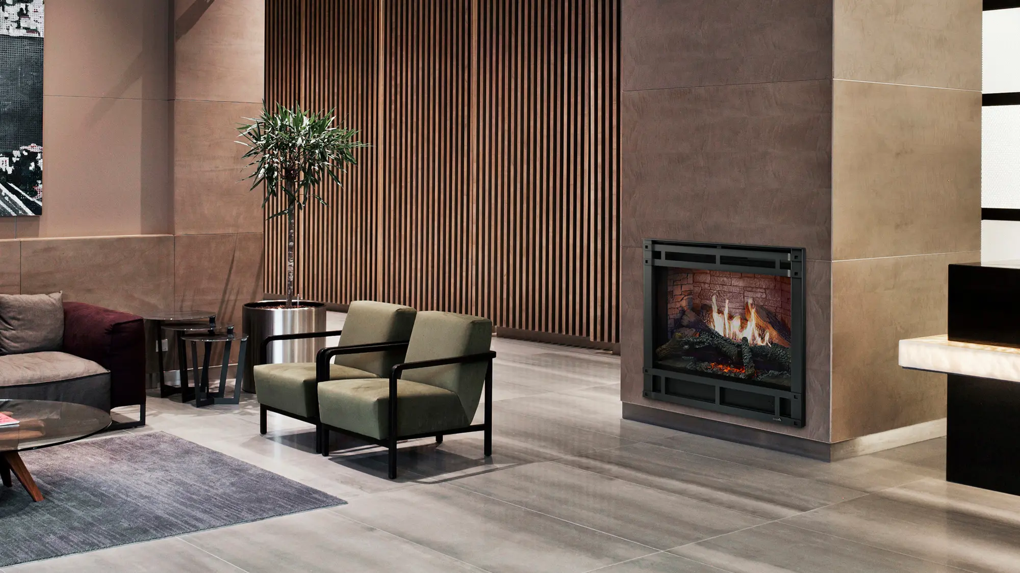 Modern living room with green chairs, a brown couch, a round coffee table, and a rectangular wooden side table. A fireplace and a potted plant add warmth to the space.