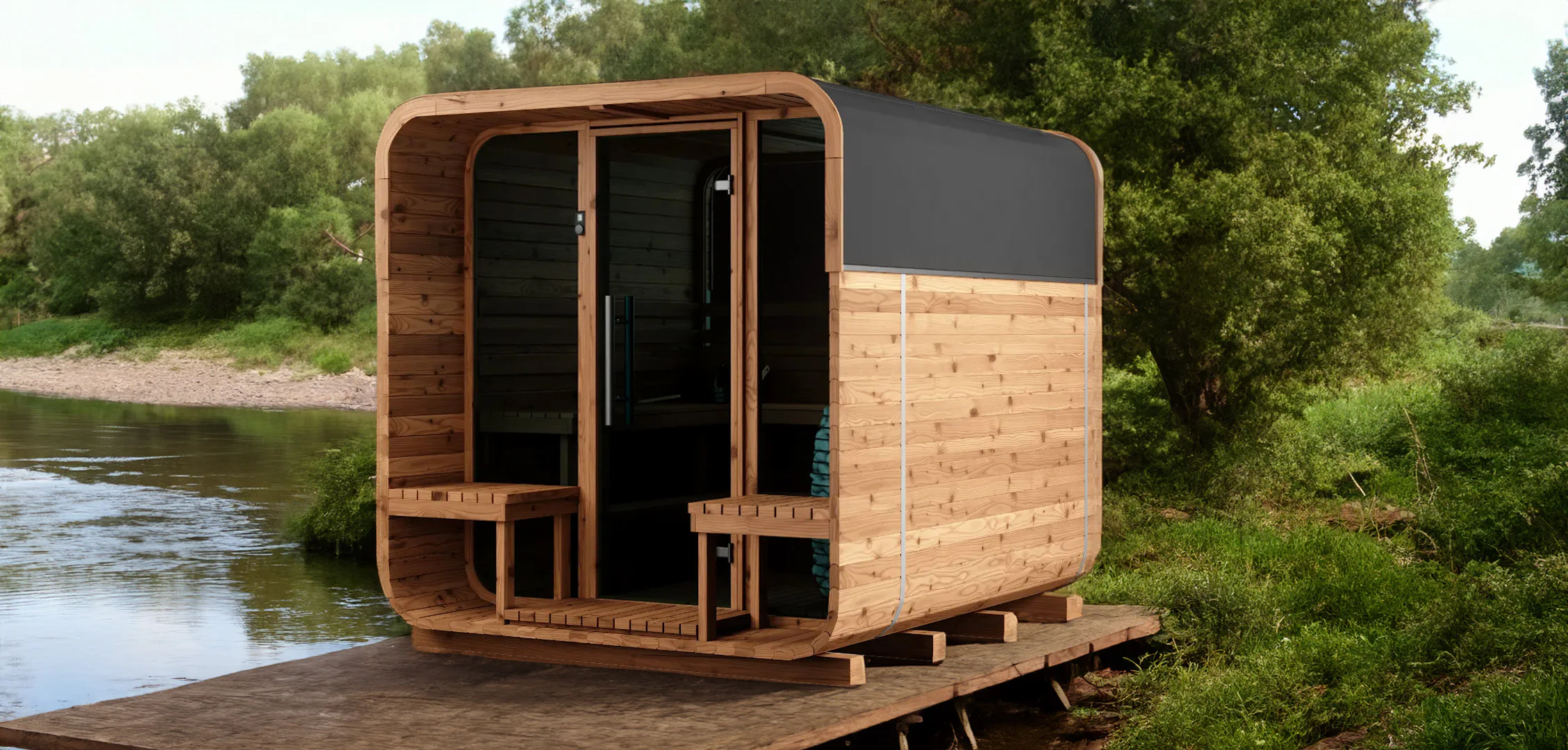 A small, modern wooden cabin with a curved design, situated on a wooden platform next to a river, surrounded by lush green trees and foliage.
