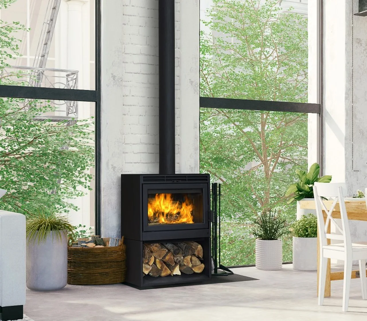 Modern living room with a black wood-burning stove, large windows, green plants, a wicker basket for firewood, and a dining table with white chairs. Indoors and outdoors blend through the glass.