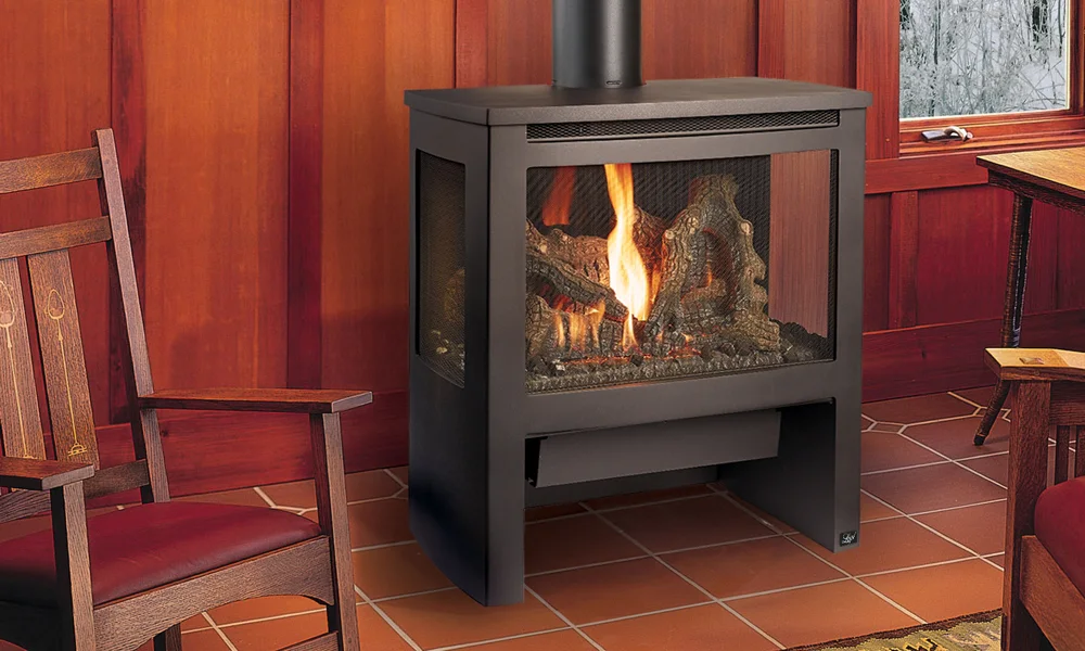 A cozy room with wood-paneled walls featuring a burning fireplace set on a tiled floor. Two wooden chairs with red cushions are positioned near the fireplace. Snow is visible through the window.