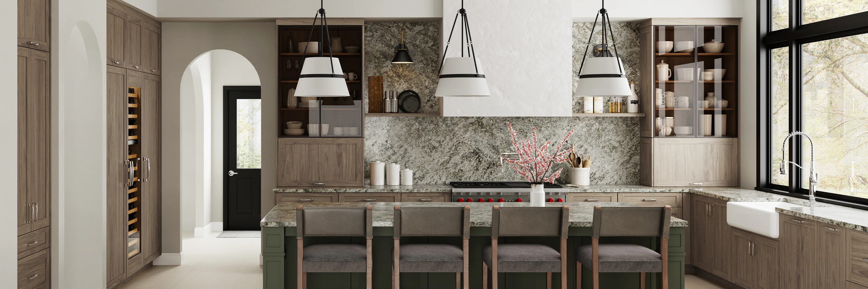 Modern kitchen with a large island, bar stools, pendant lights, and gray cabinets. A gas range with red knobs is centered under a range hood, and there is a farmhouse sink by large windows.