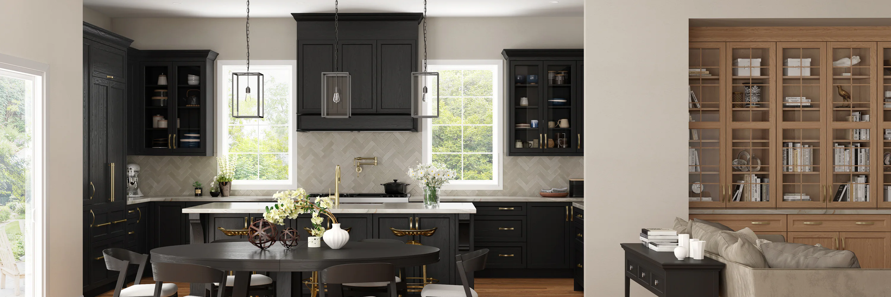 Modern kitchen with black cabinets, gold accents, and two large windows with green views. A round dining table with decor in the foreground and a wooden bookshelf in the background.