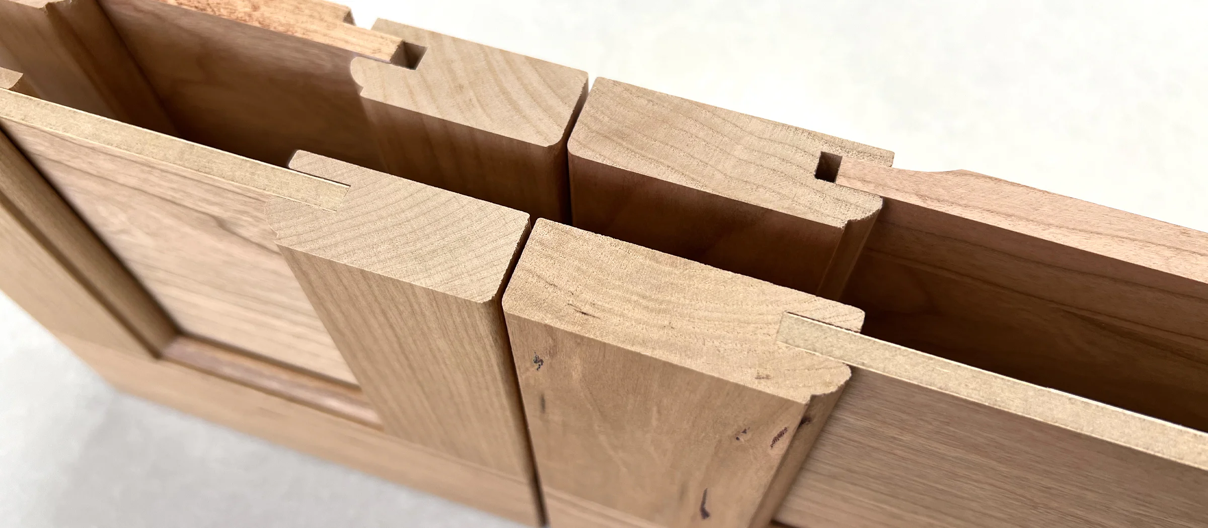 Close-up of interlocking wooden joints, showing precise dovetail construction with smooth, natural wood grain. The joints create a strong, seamless connection.