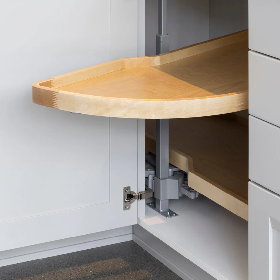 Half-moon light-wood pull-out shelf extended from an open white corner kitchen cabinet, showing metal pivot mechanism
