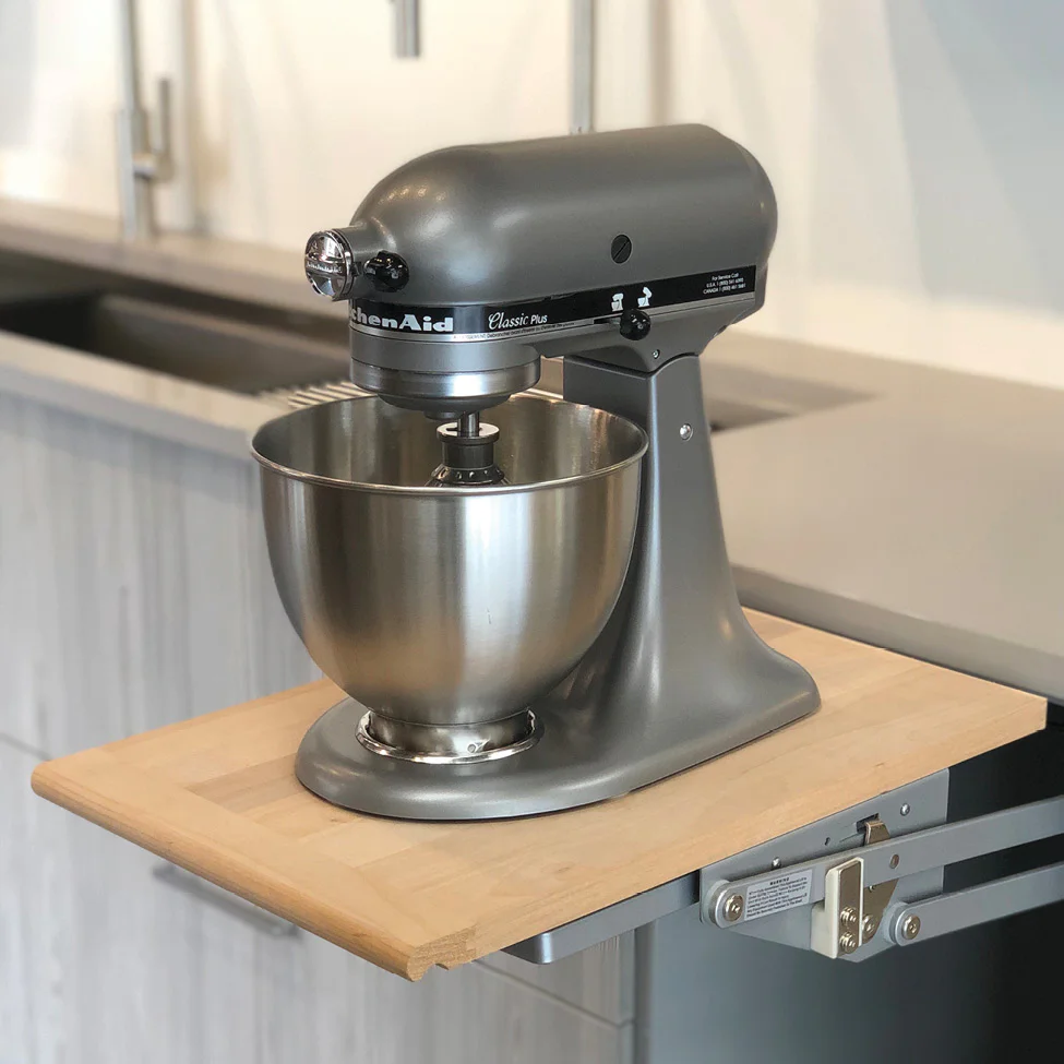Gray KitchenAid Classic Plus stand mixer with stainless steel bowl on a wooden pull-out counter in a modern kitchen.