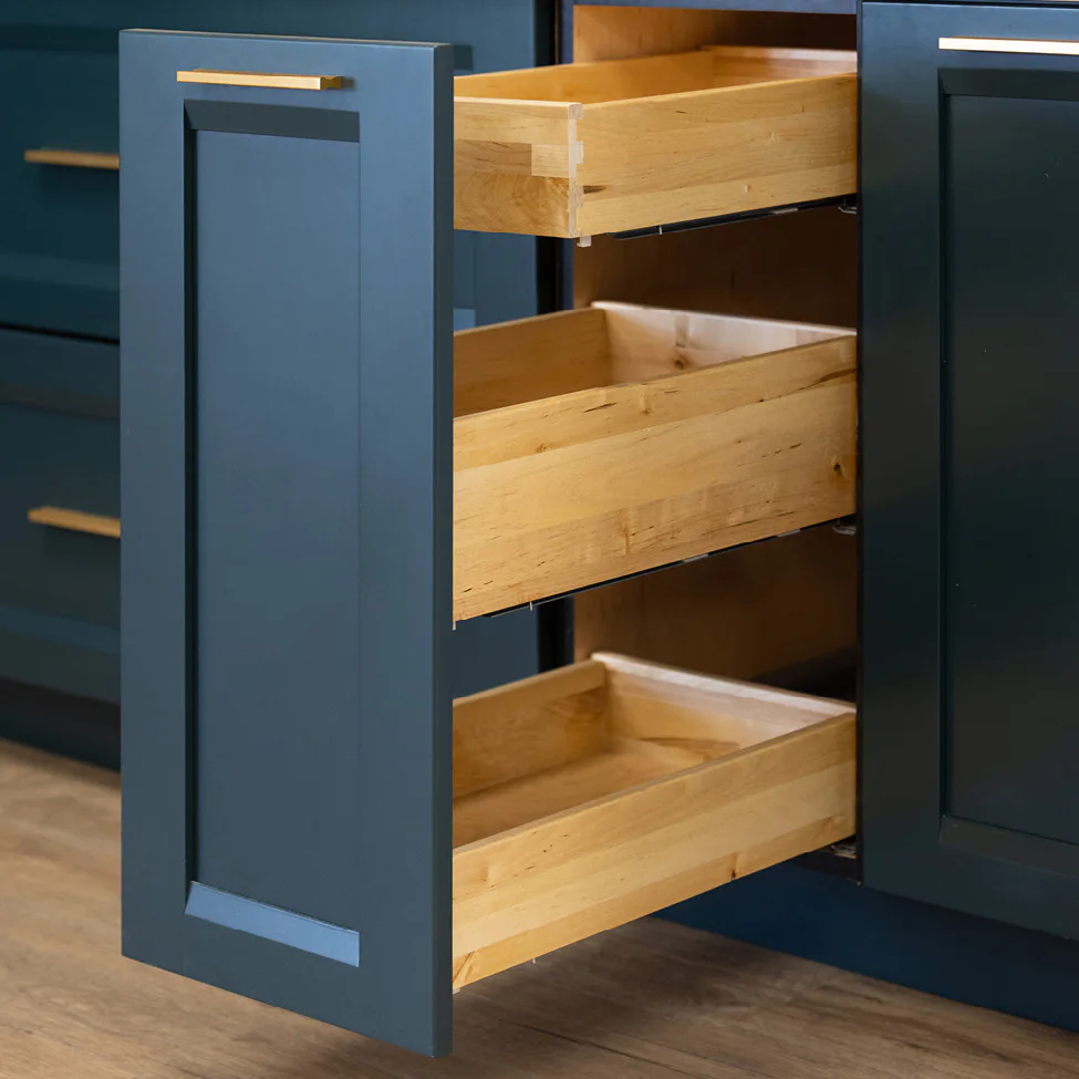 Open dark-blue kitchen cabinet showing three wooden pull-out drawers and brass handles