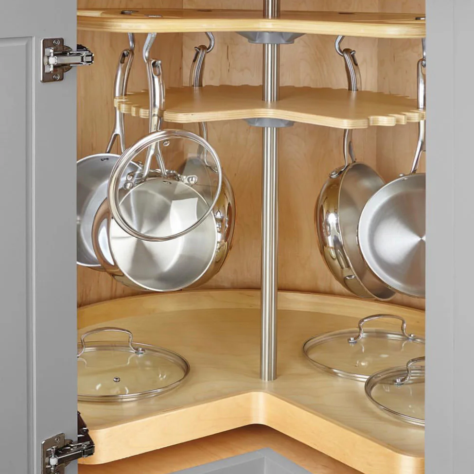 Open corner kitchen cabinet with rotating wooden lazy Susan storing stainless steel pots and glass lids