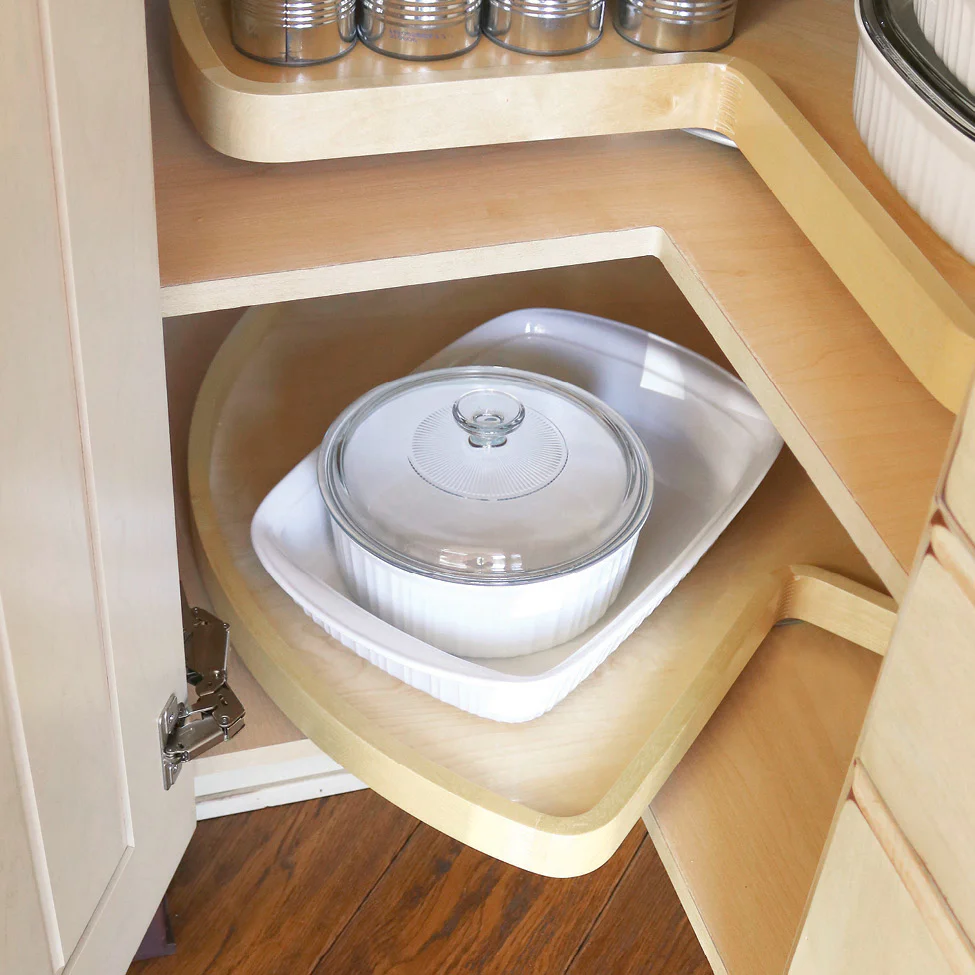 Corner kitchen cabinet with a pull-out wooden shelf holding white baking dishes and a glass-lidded casserole dish.