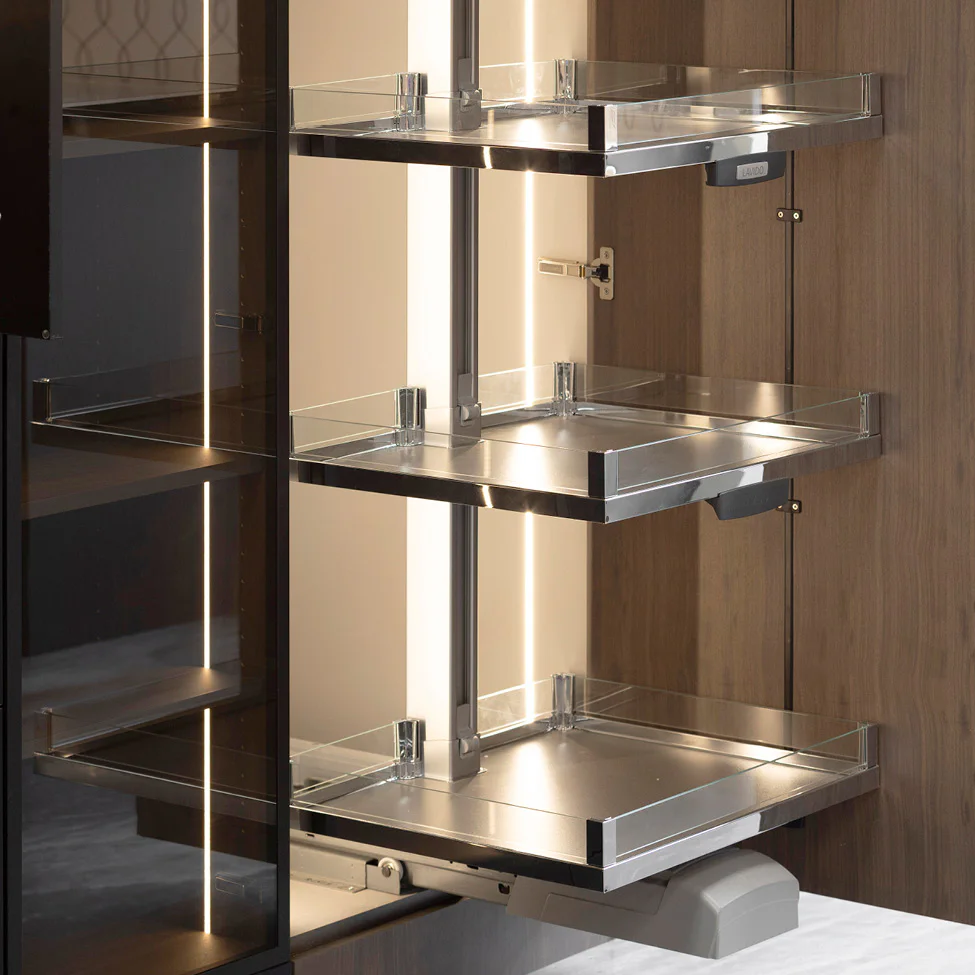 Three chrome pull-out pantry shelves with glass guards inside a wooden kitchen cabinet lit by a vertical LED