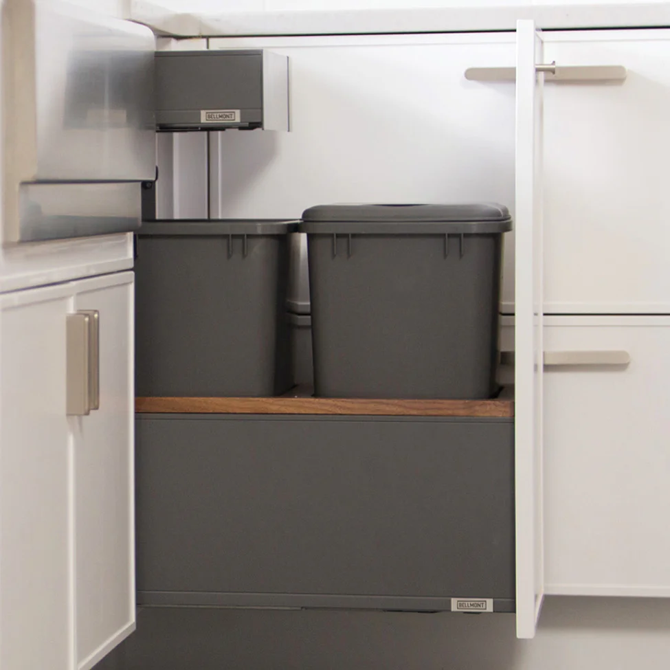 Open kitchen cabinet under sink with two gray plastic pull-out bins on a wooden shelf