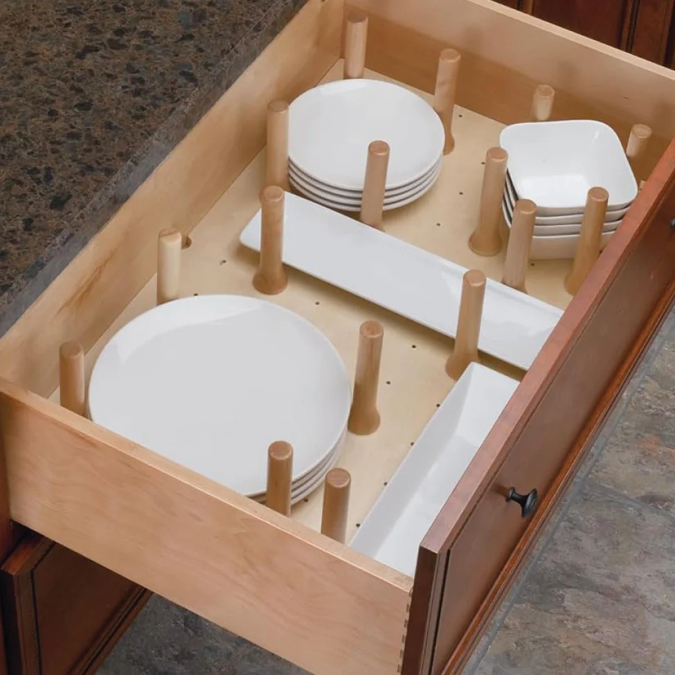 Open kitchen drawer with wooden peg organizer holding stacked white plates and rectangular serving dishes