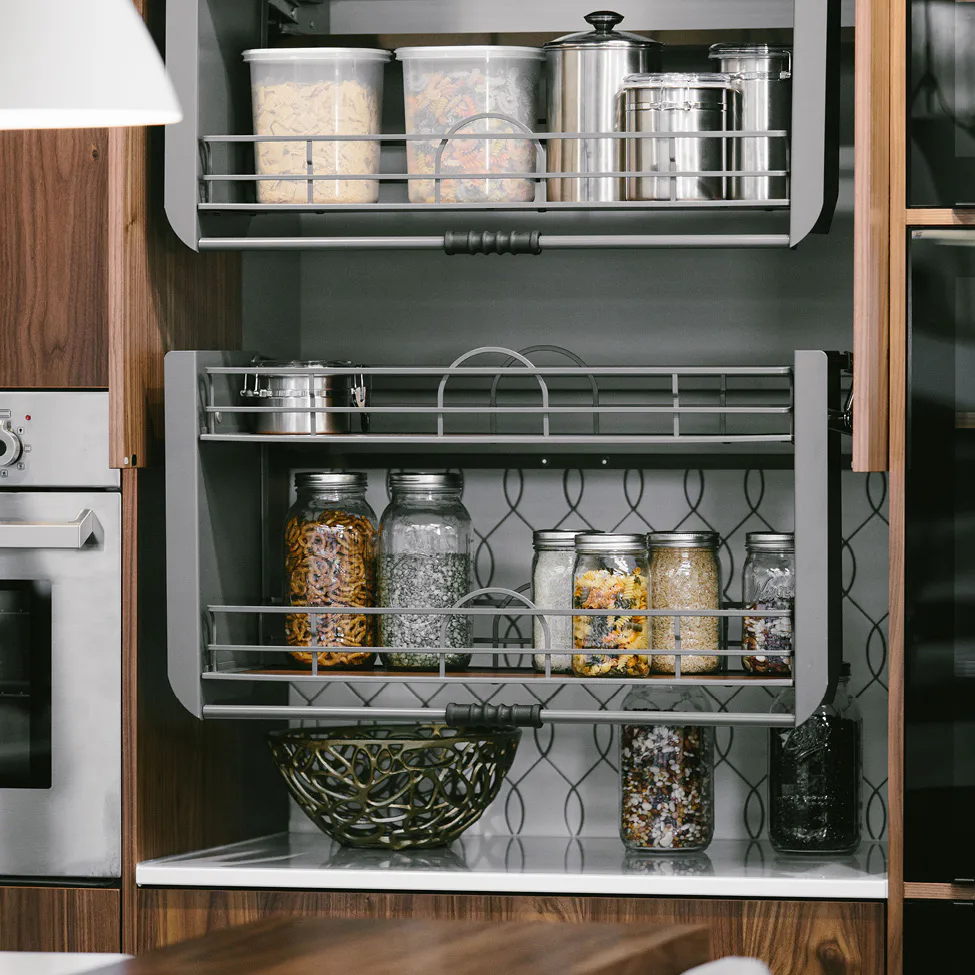 Pull-out kitchen shelves with glass jars, metal canisters and storage containers in wooden cabinet