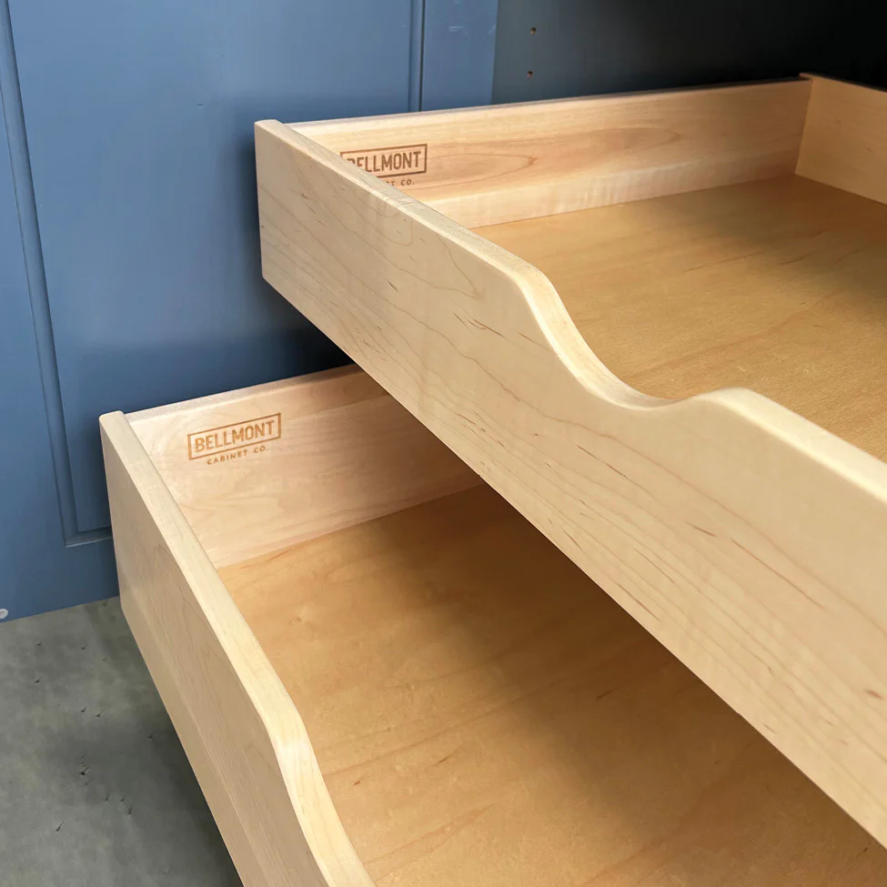 Two open light wood drawers with scalloped fronts and 'Bellmont' stamp against a blue cabinet