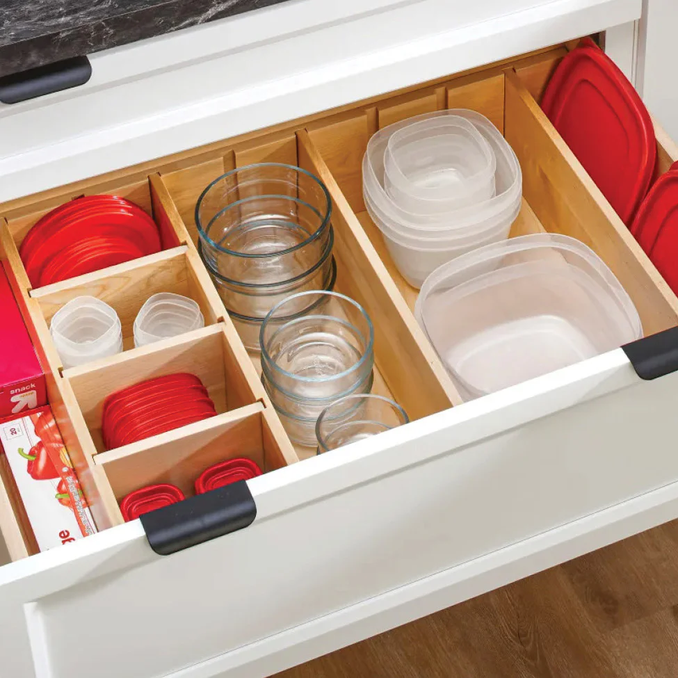 Open kitchen drawer with wooden dividers organizing glass bowls, plastic food storage containers and red lids