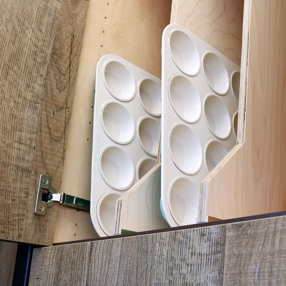 Two white plastic paint palettes with round wells stored upright in a wooden cabinet divider