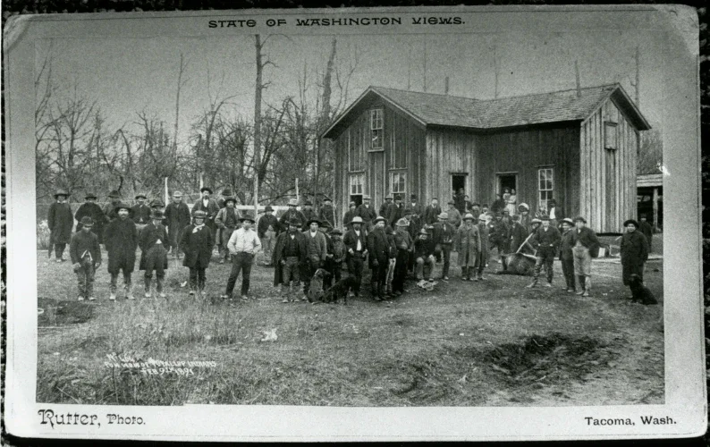 Black-and-white historic group portrait of men and boys standing outside a wooden building in Tacoma, Washington.