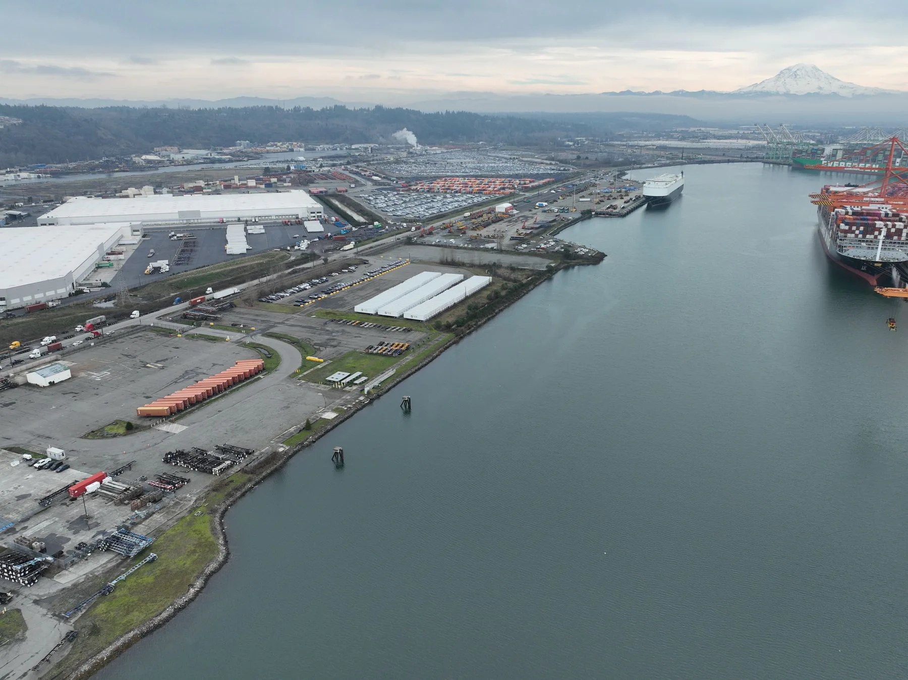 Aerial view of a port with container ships, cranes, warehouses and cargo yards by the water.