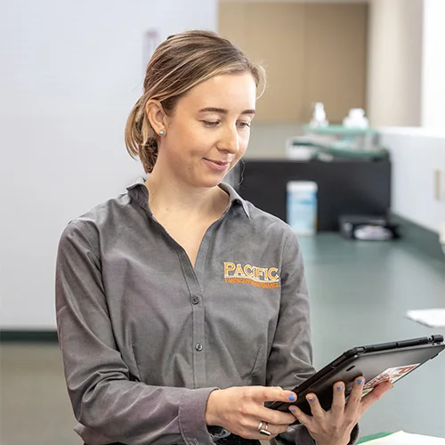 A woman wearing a Pacific University shirt is using a tablet in an indoor setting with a green countertop in the background.