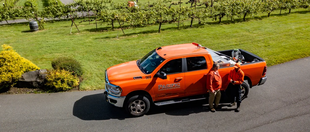 Two people in orange jackets stand beside a bright orange truck marked 