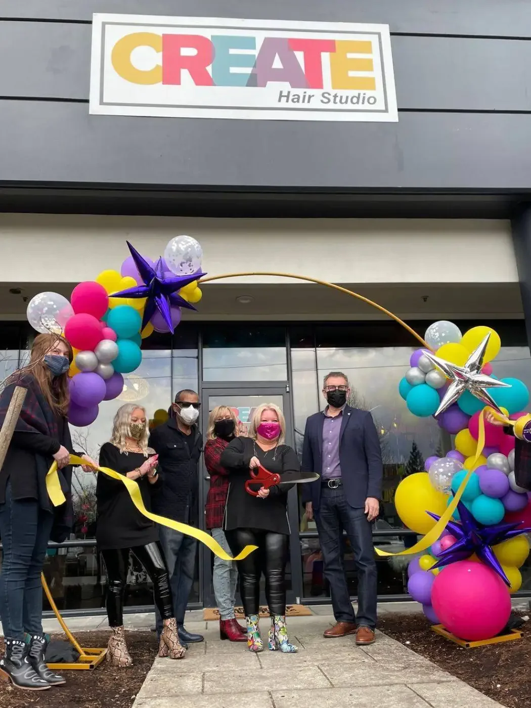 Group of people wearing masks participate in a ribbon-cutting ceremony outside 