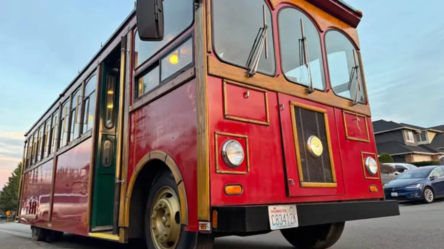 Front-side view of a red vintage trolley bus with wooden trim parked on a suburban street