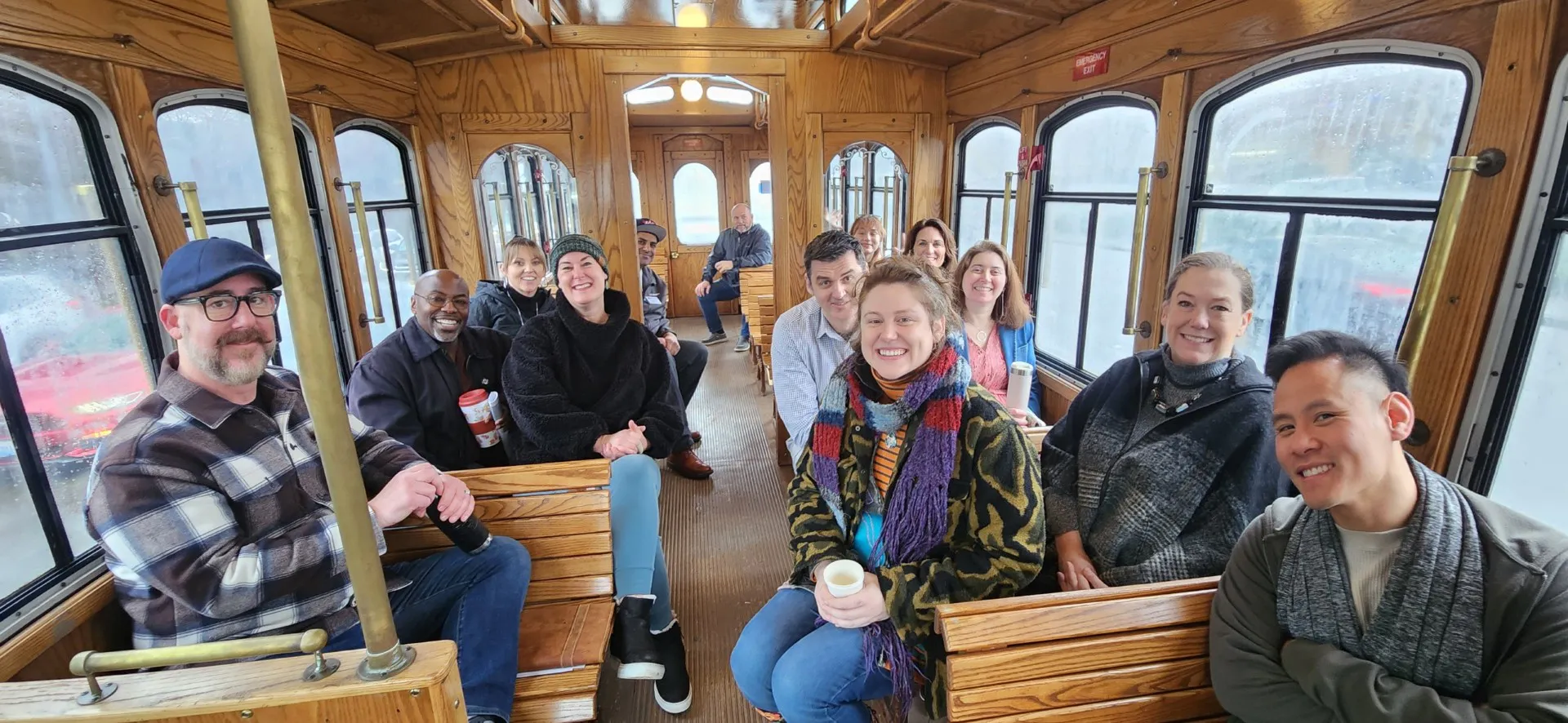 Group of smiling adults seated inside a wooden vintage trolley car