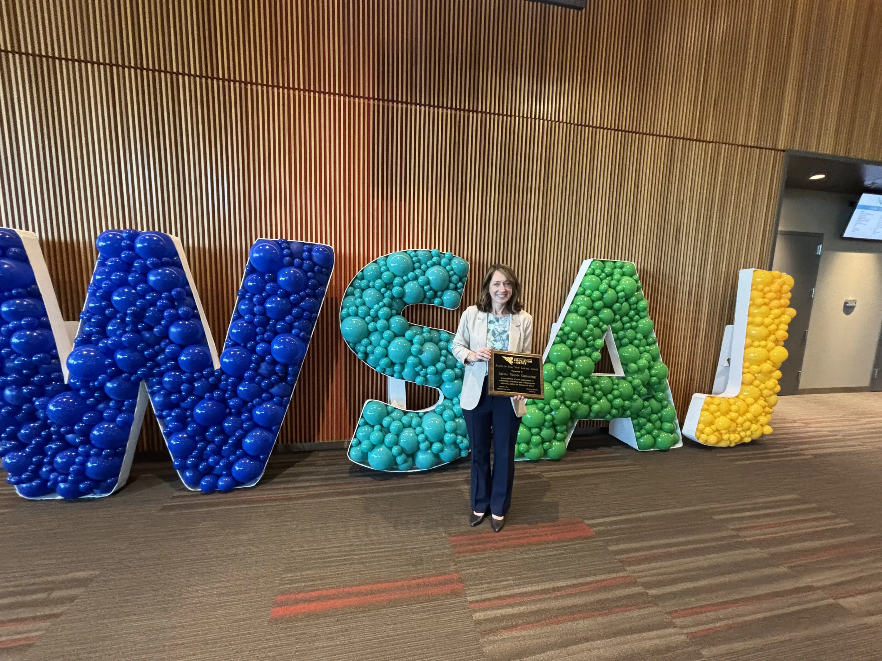 A person holding a plaque stands in front of large balloon letters spelling 