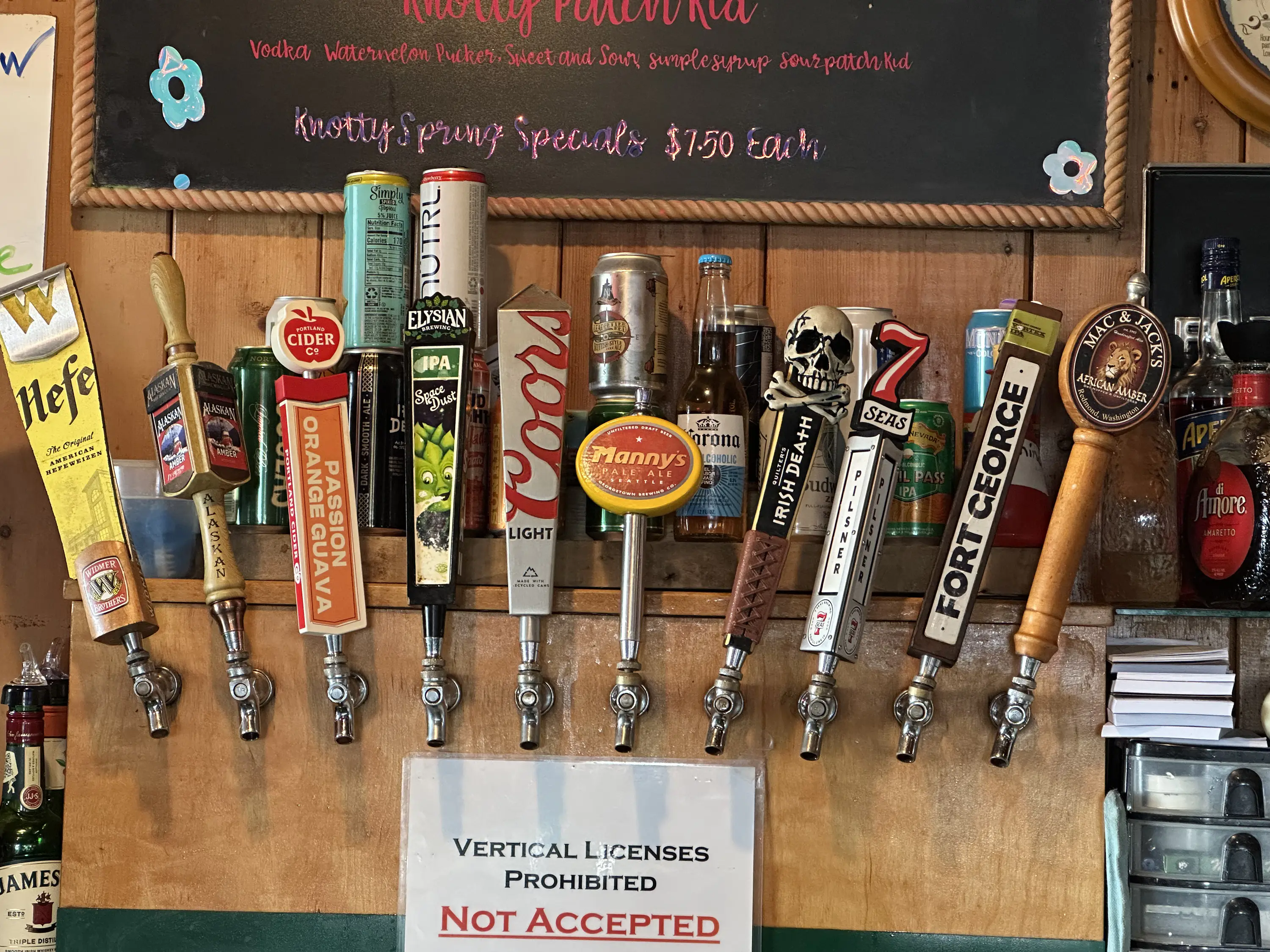 Draft beer taps with various branded handles are lined up above a sign stating 