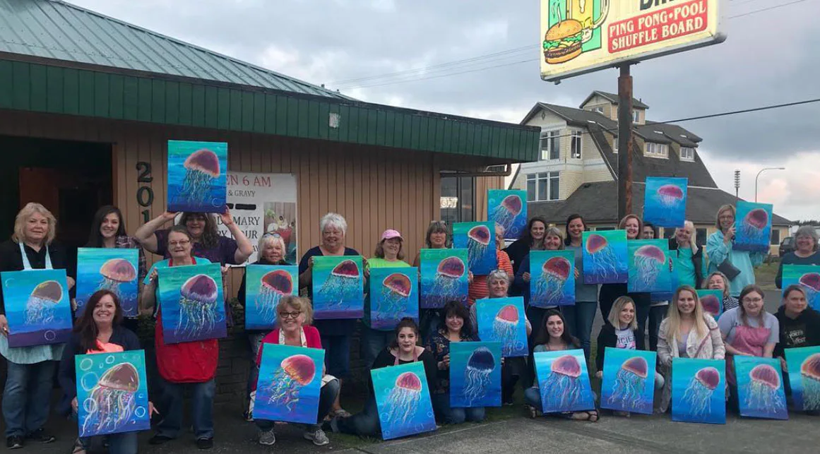 A group of people standing outside a building, each holding a colorful painting of a jellyfish. A sign above reads 