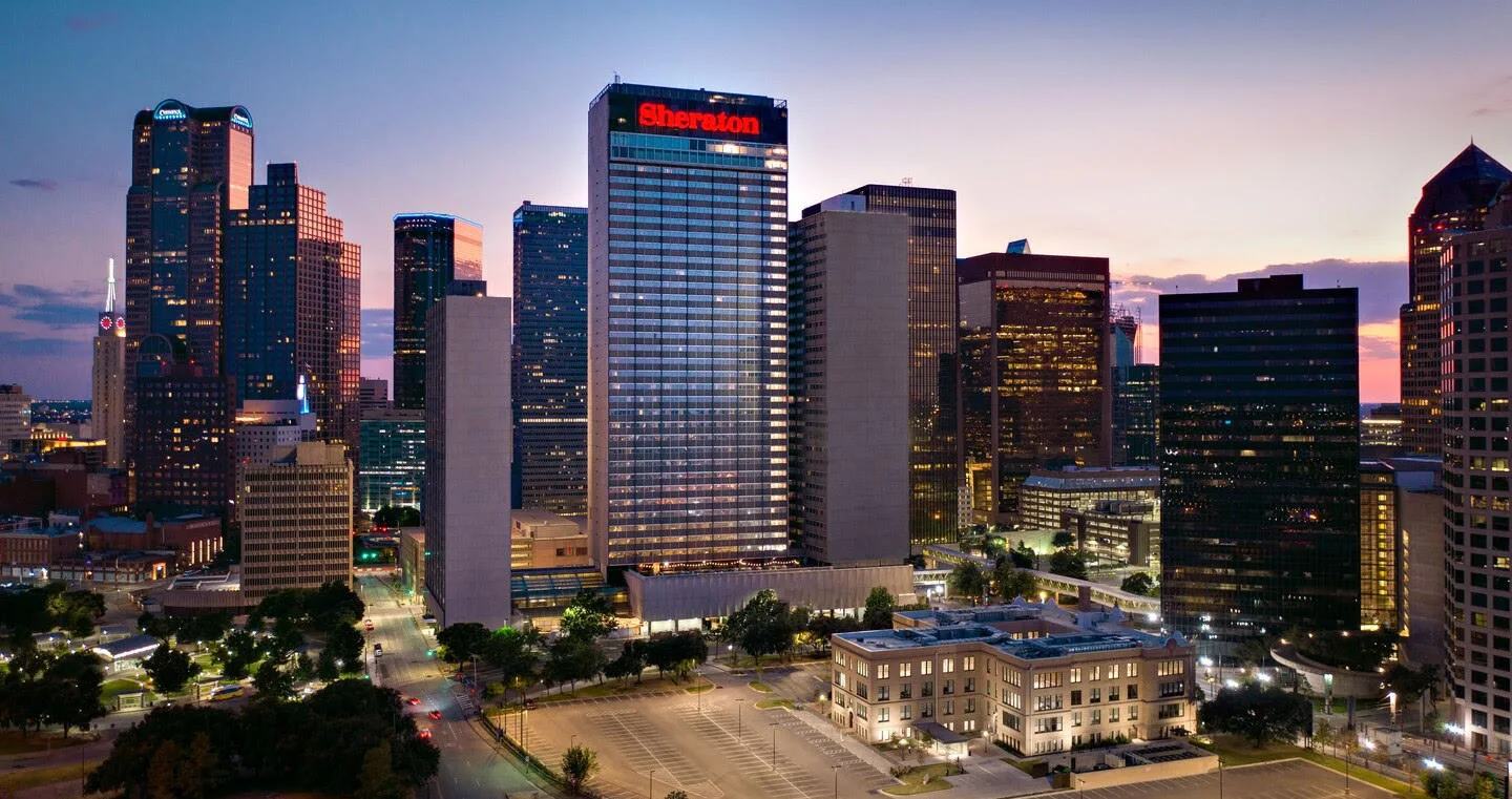 Downtown skyline at dusk with Sheraton hotel tower centered among illuminated skyscrapers and streets below