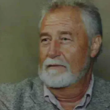 A bearded man in a gray blazer, looking thoughtful