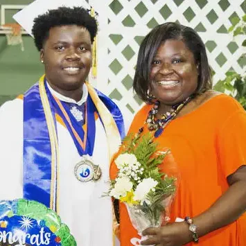 A graduate in cap and gown beside a smiling woman holding flowers