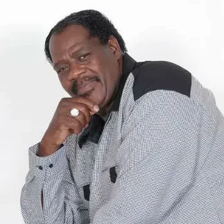 A man in a checkered suit, seated and smiling